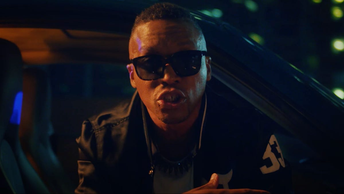 Lupe at the window of a Porsche in his 2022 AUTOBOTO video. I’m keeping the actual artist and car beside the driver image; this later scene is a visual companion to the 2007 song.